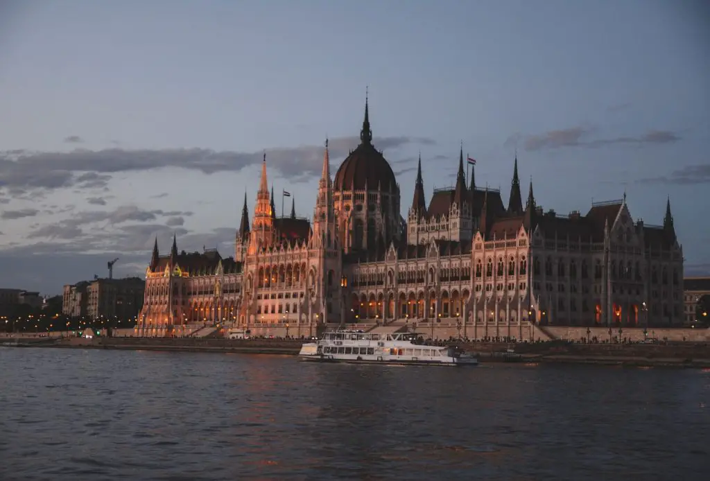 a large building with towers and a boat in front of it with Hungarian Parliament Building in the background